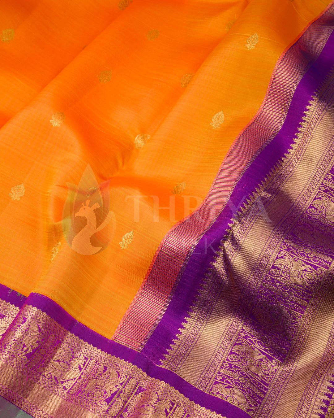 close up of bright orange silk saree with golden motifs and rich purple zari border