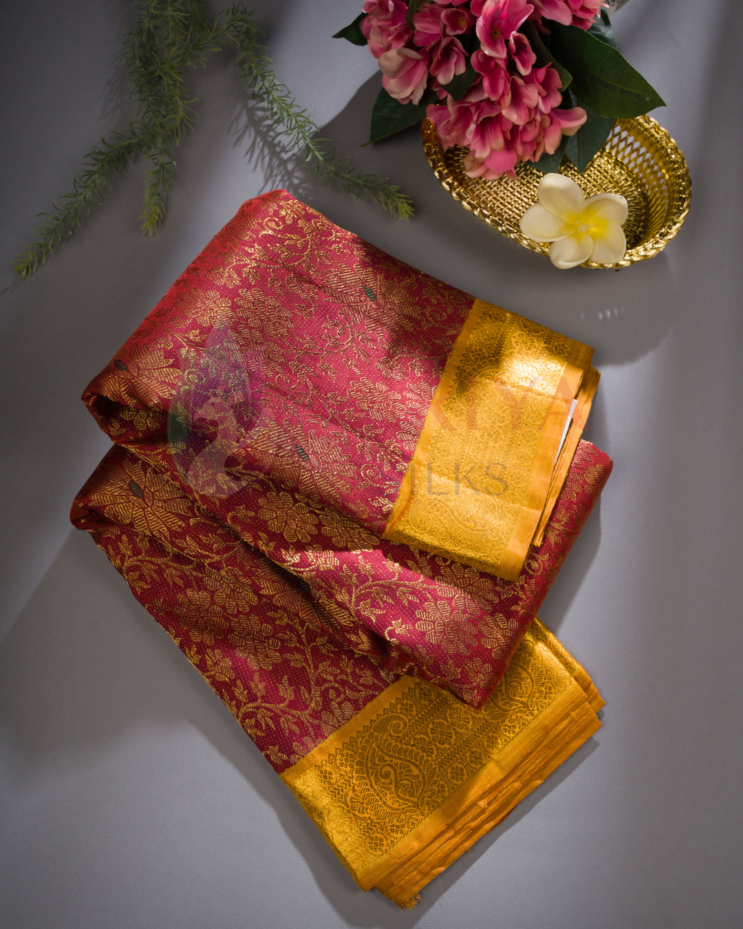 Maroon Kanjivaram silk saree with golden zari border, styled with flowers on a grey background.