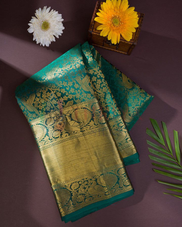 Folded green Kanjivaram saree with traditional gold zari detailing – flatlay with flowers