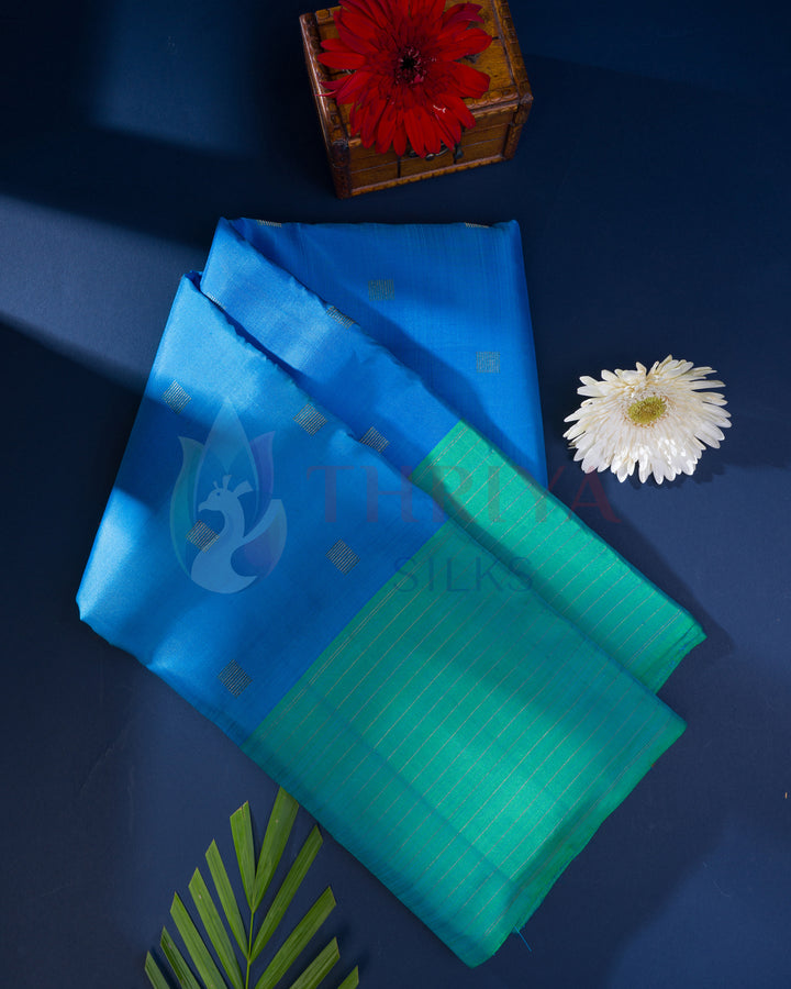 Folded blue and green silk saree with golden zari polka dots and border – styled flatlay