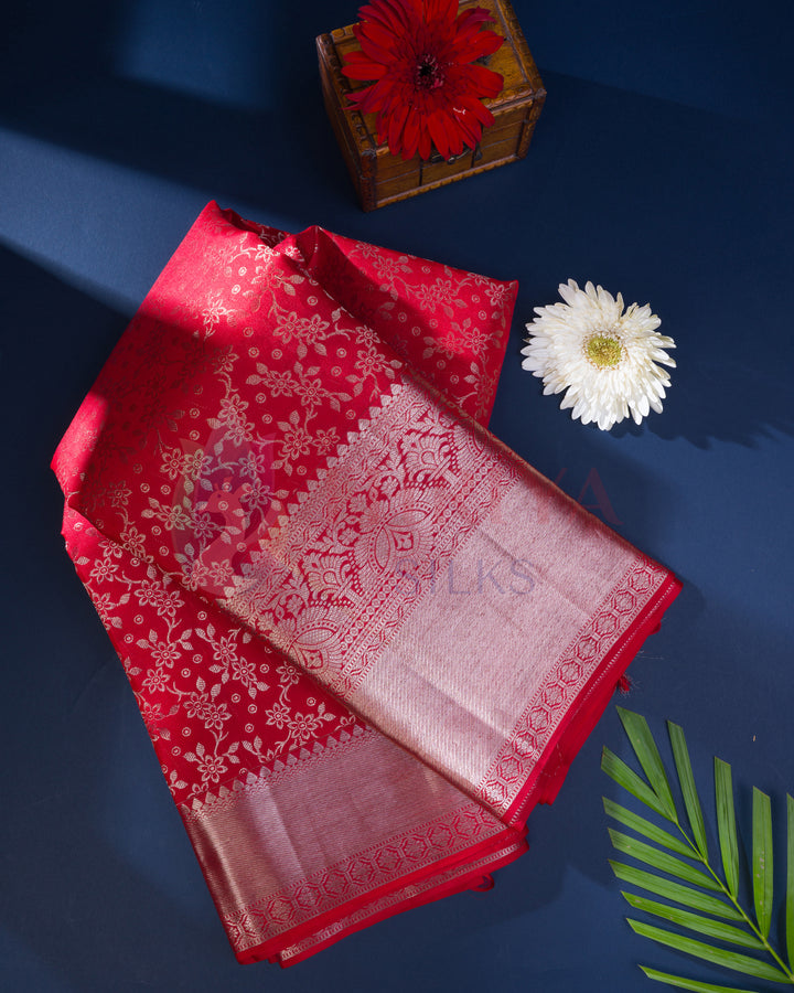 Folded red Kanjivaram silk saree with silver floral zari work, styled with flowers and a wooden box
