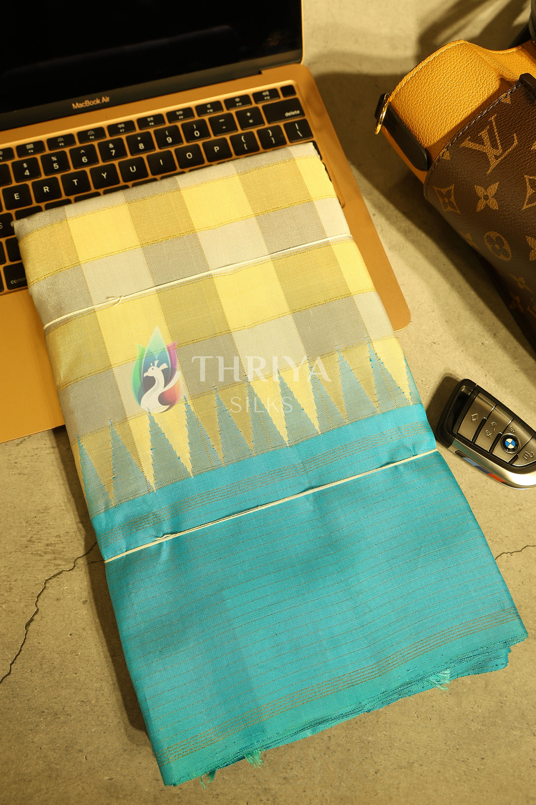 Folded aqua blue silk saree with yellow checks shown in luxury modern setup.
