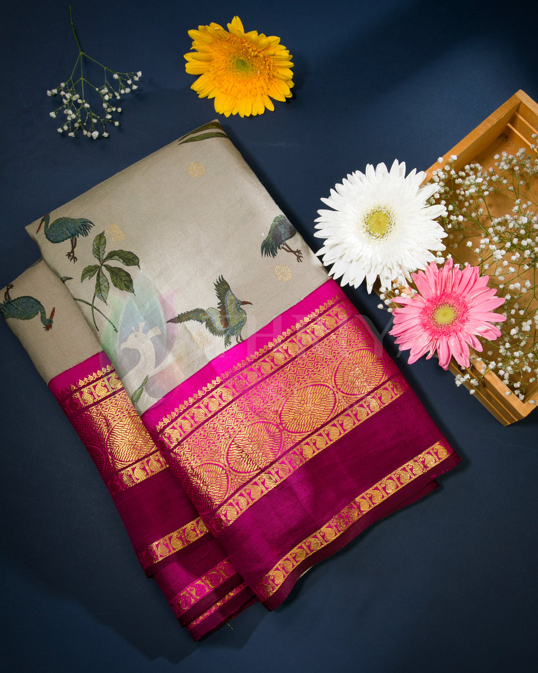 Folded view of beige silk saree featuring colorful bird motifs and a vibrant pink-gold zari border.