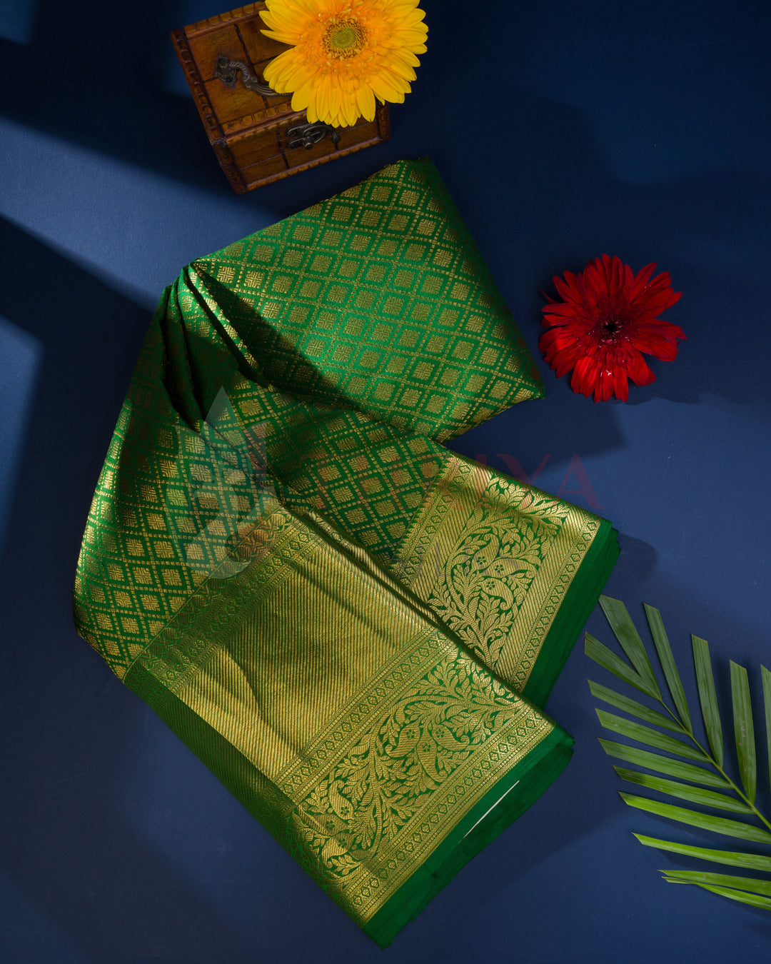 Green Kanchipuram silk saree with gold zari, styled with red flower and blue backdrop