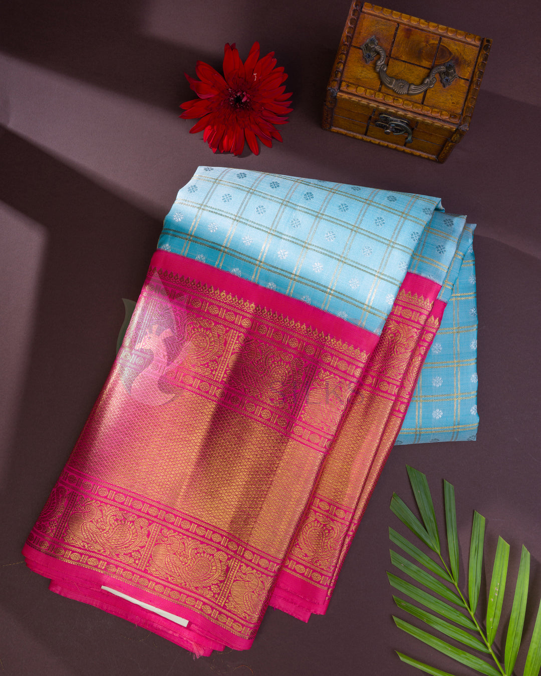 Bridal Kanchipuram silk saree in pink and blue with gold zari, styled with red flower, gift box, and leaves