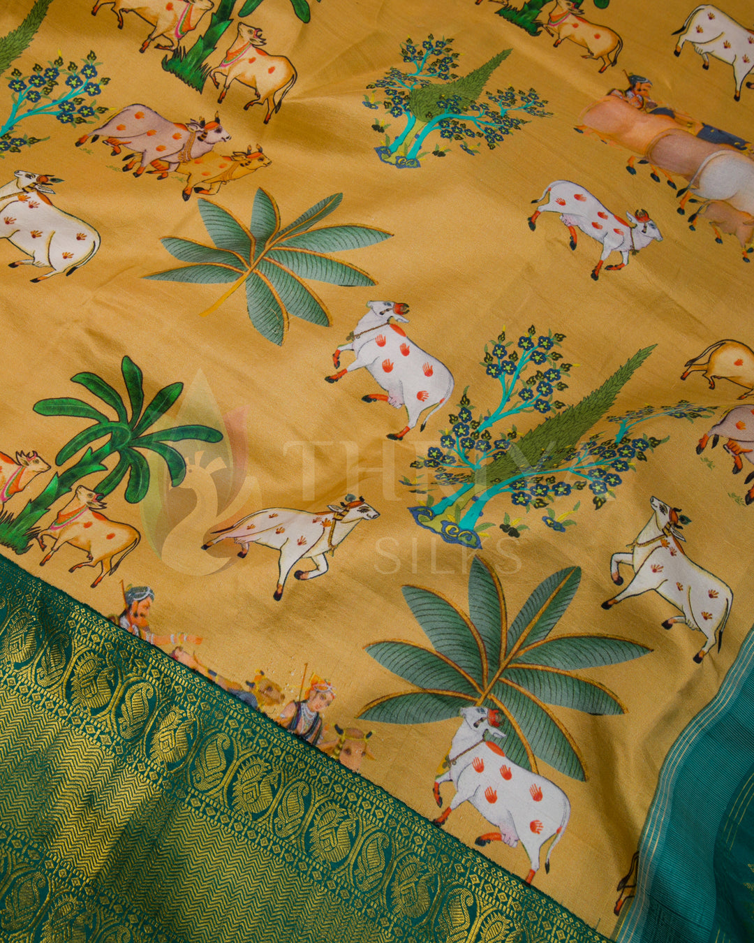 Close-up of the cow and palm leaf motifs with intricate green zari border on mustard silk fabric