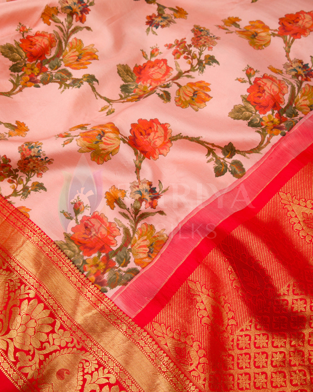 Close-up showing detailed rose floral patterns on the blush pink body with contrast red pallu and zari work.
