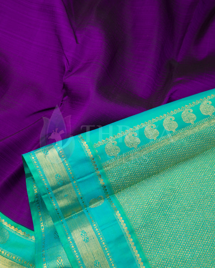 Close-up view showing rich purple silk body and aqua blue pallu with golden motifs