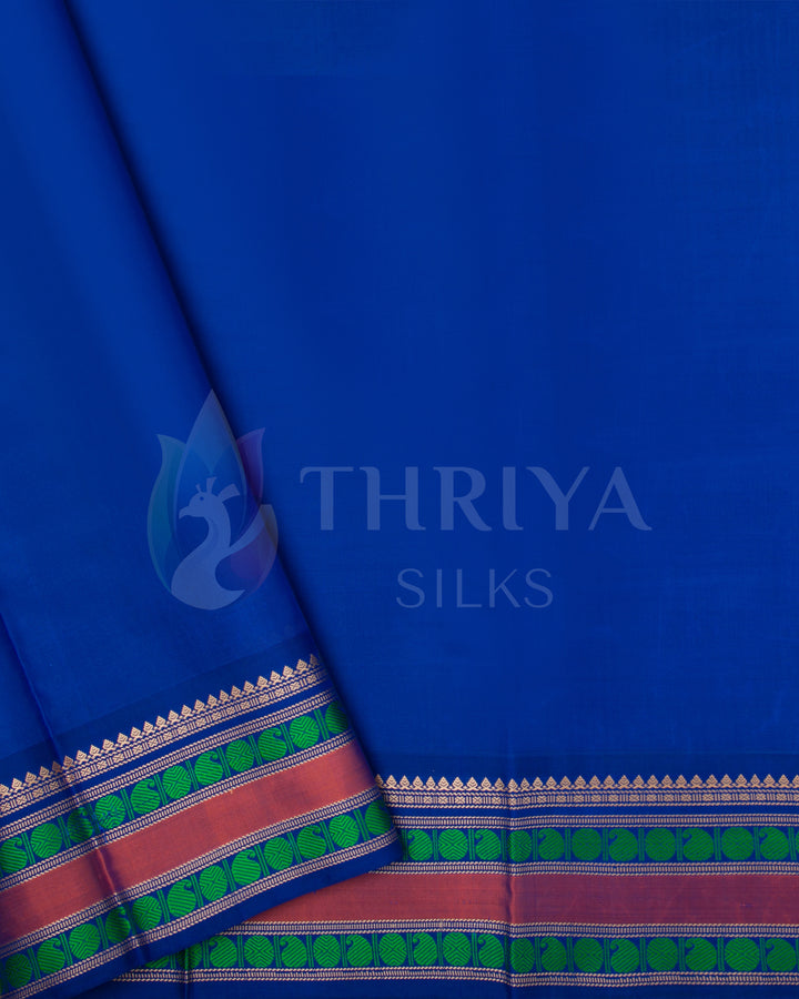 Contrasting royal blue blouse piece with pink and green zari border designed to match the green silk saree.