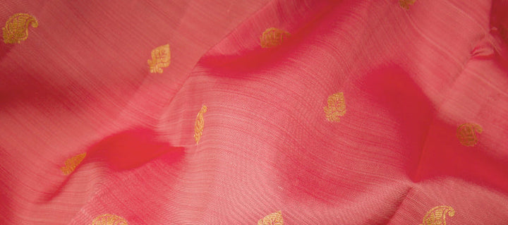 Close-up of coral pink saree fabric featuring small gold zari paisley motifs
