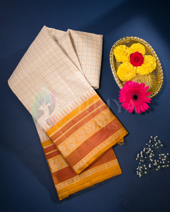 Cream silk saree with orange zari border styled with festive flowers on blue backdrop