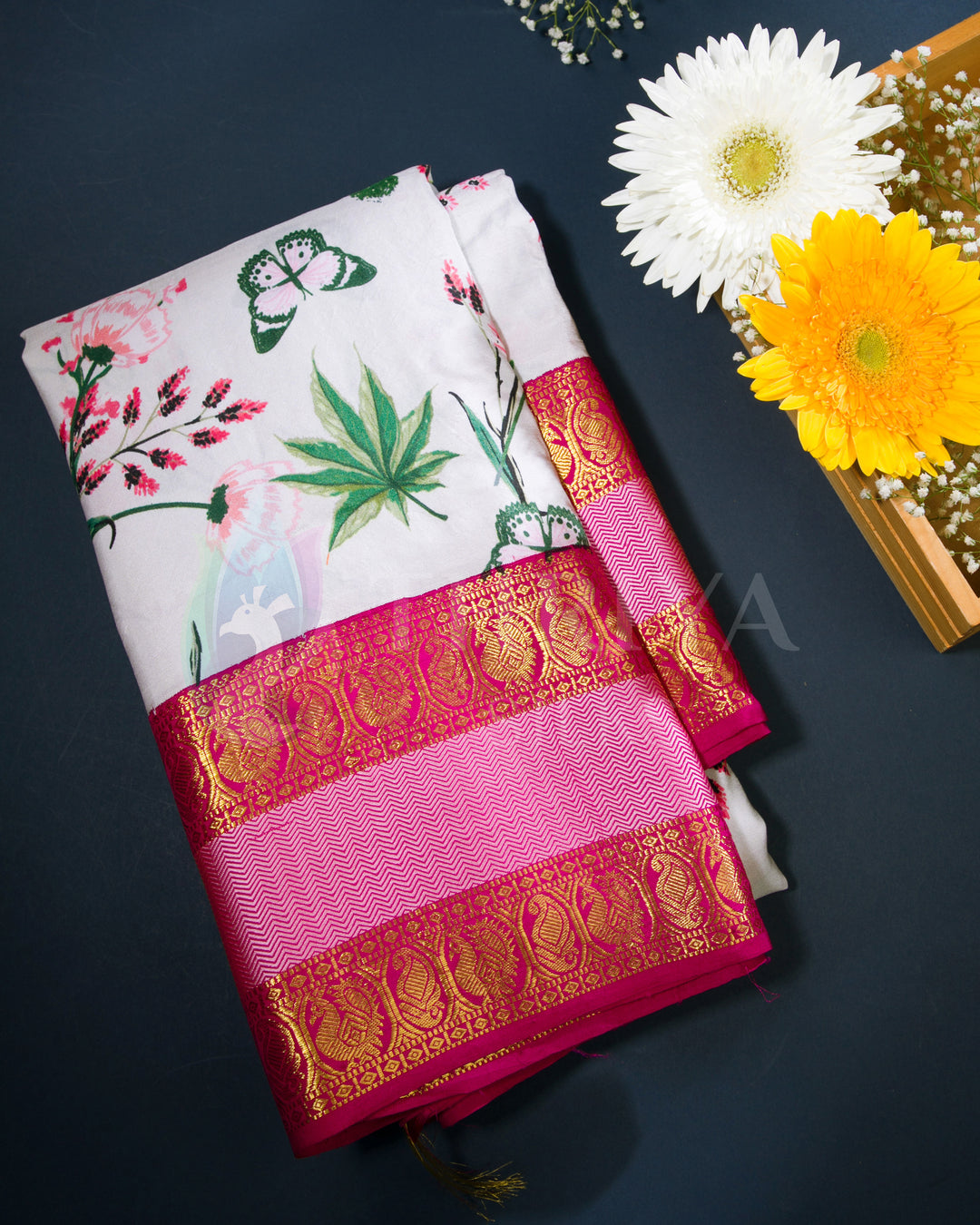 Folded Kanchipuram silk saree featuring floral print body and rich pink-gold zari border, displayed with fresh flowers.