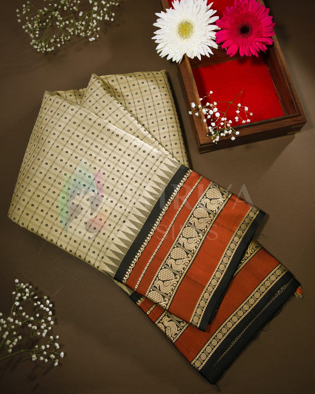 Folded view of beige silk saree with rust-orange and black zari border, styled with decor from Thriya Silks