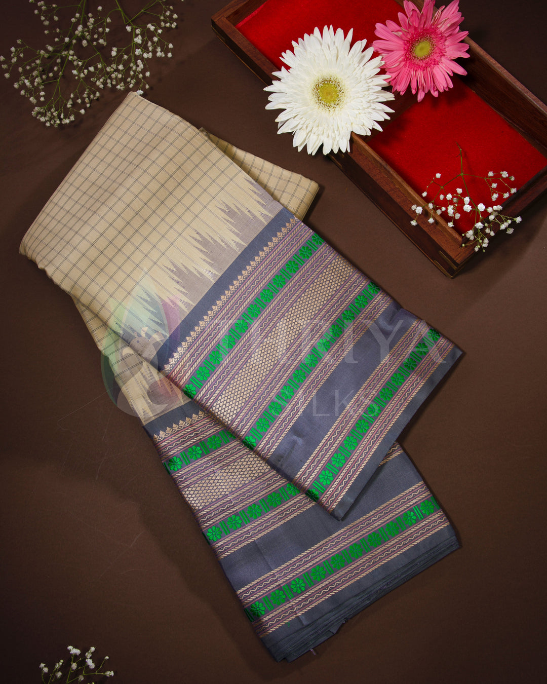 Folded beige and grey silk saree with green zari detailing – styled flatlay with flowers from Thriya Silks