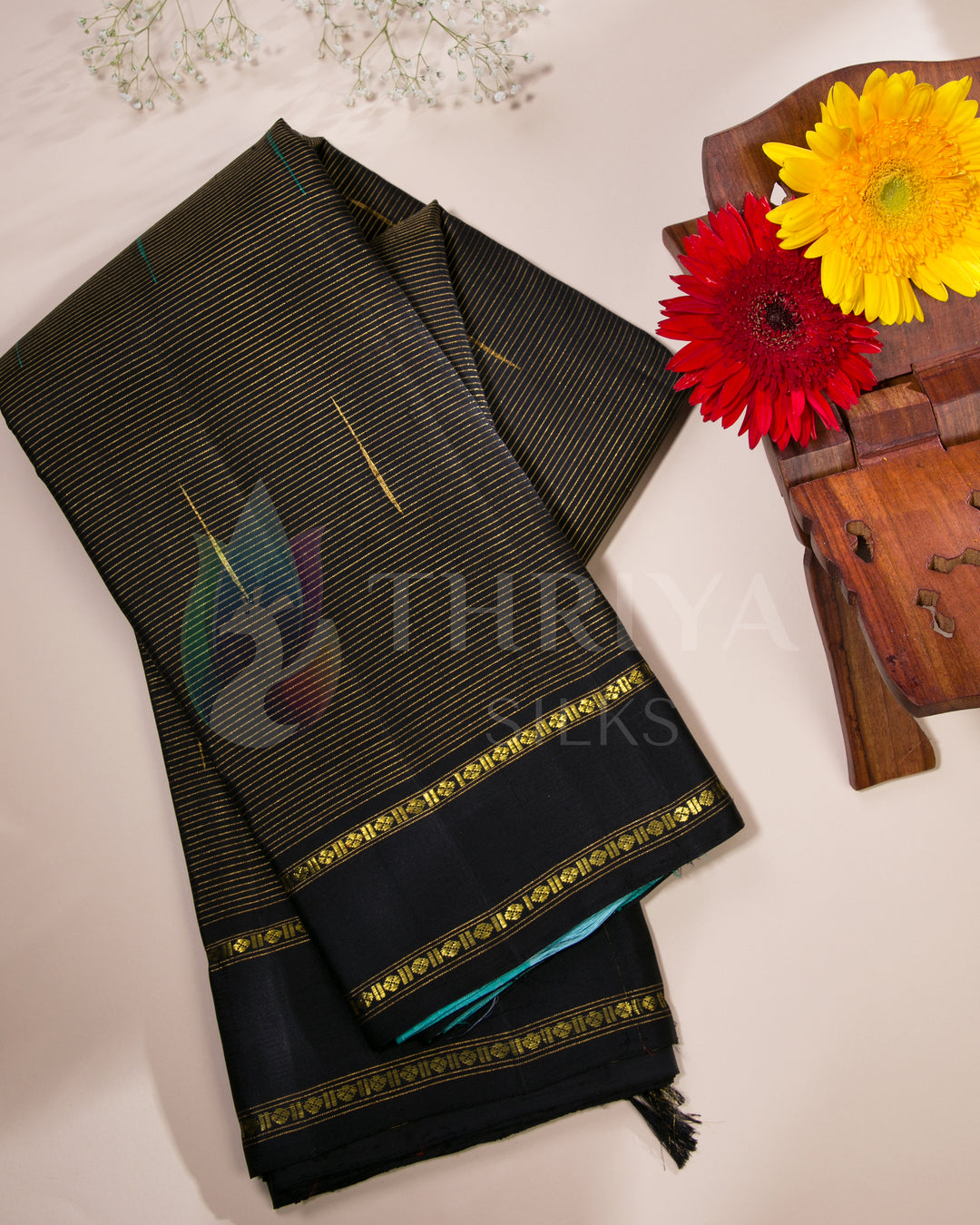 Folded Thriya silk saree in black and turquoise with floral flat lay setup for festive styling