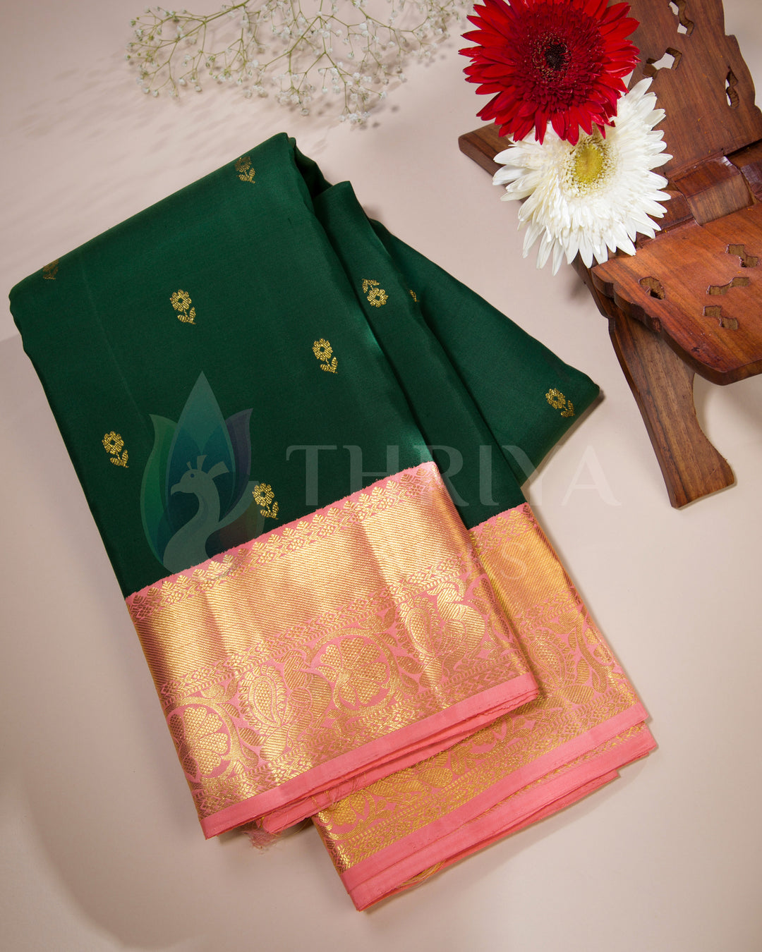 Folded green silk saree with peach-gold border styled with flowers for festive flat lay