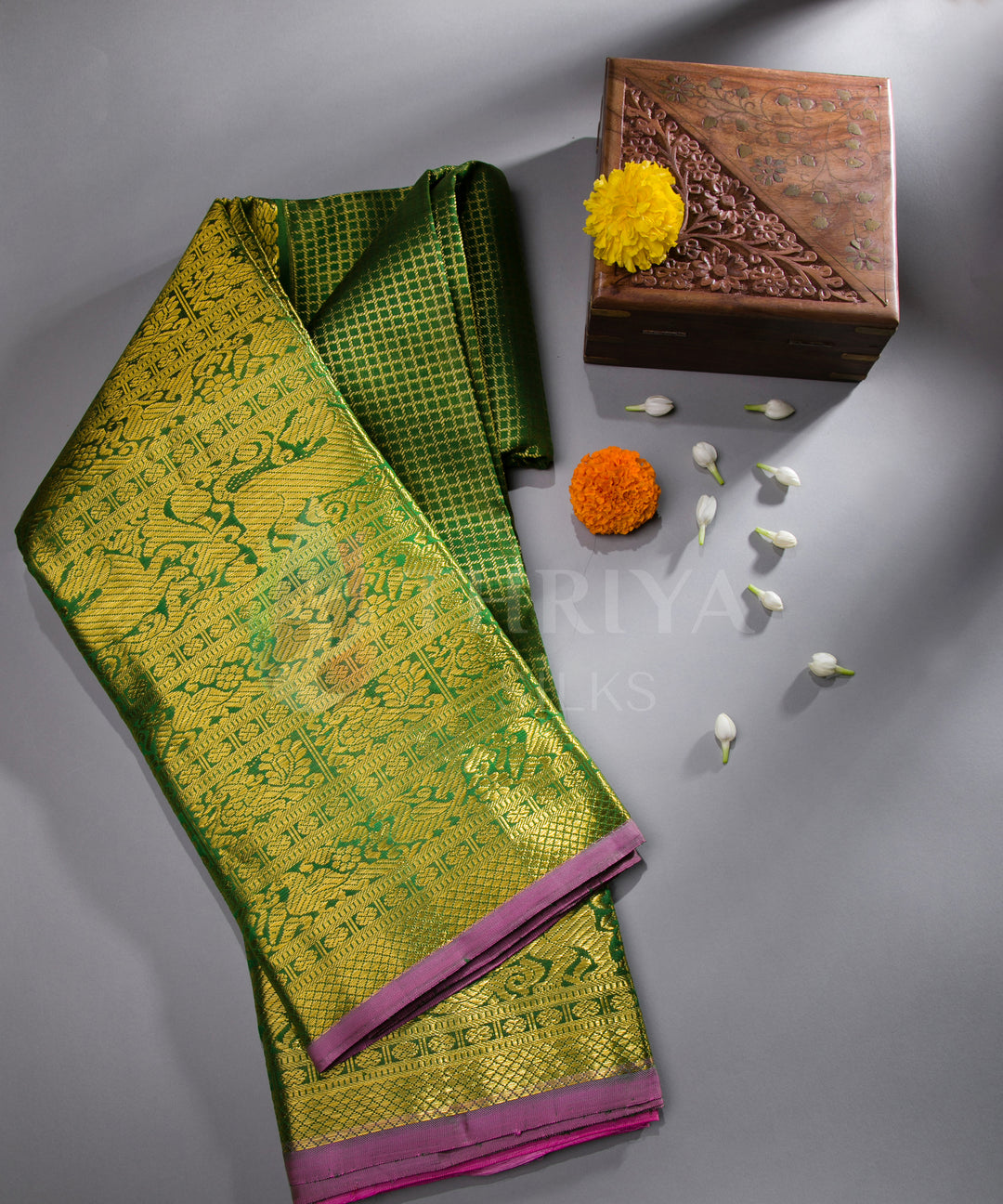 Folded green Kanchipuram silk saree with pink border in a flatlay style, adorned with decor