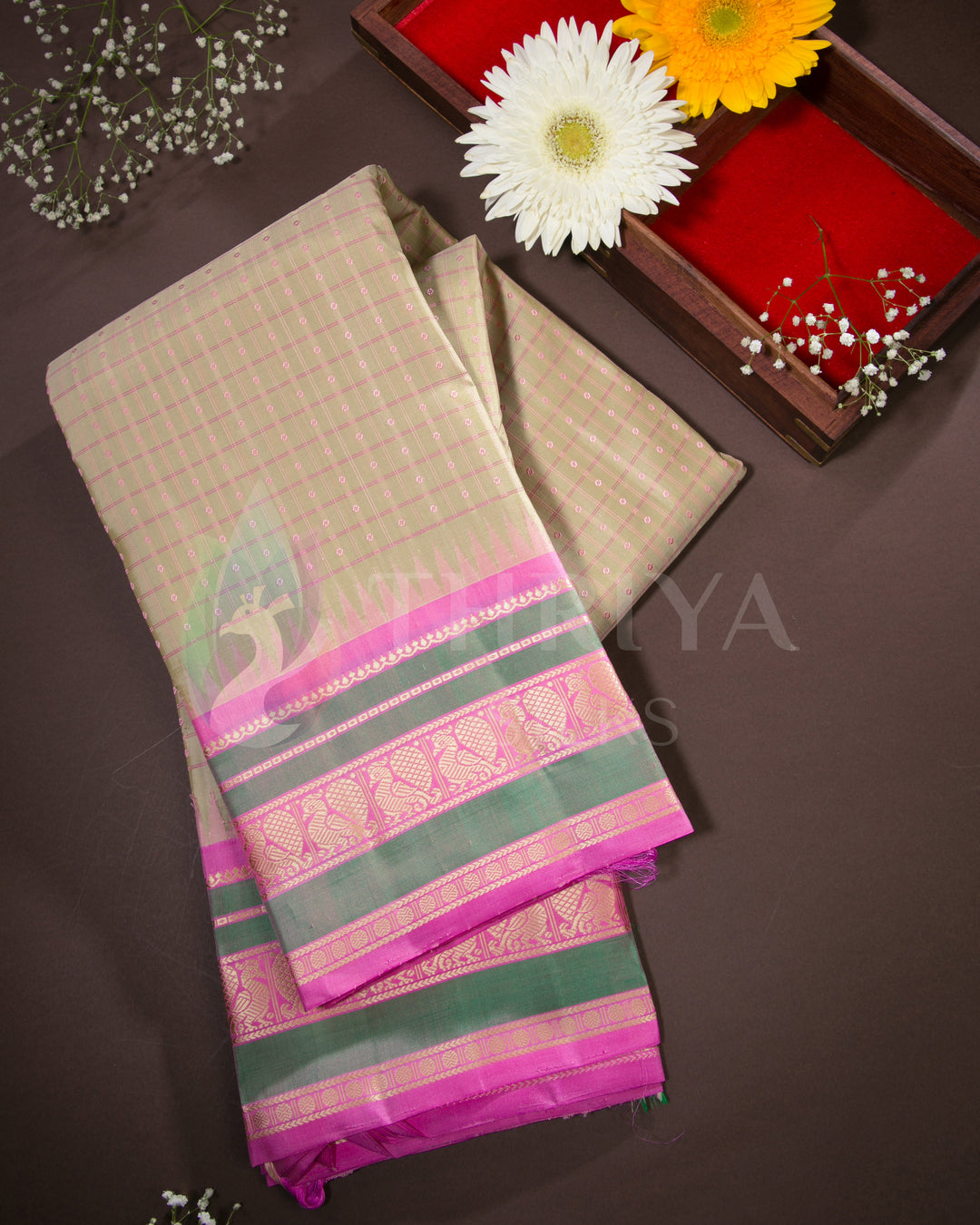 Folded beige and pink Kanjivaram silk saree with green zari border, styled with flowers