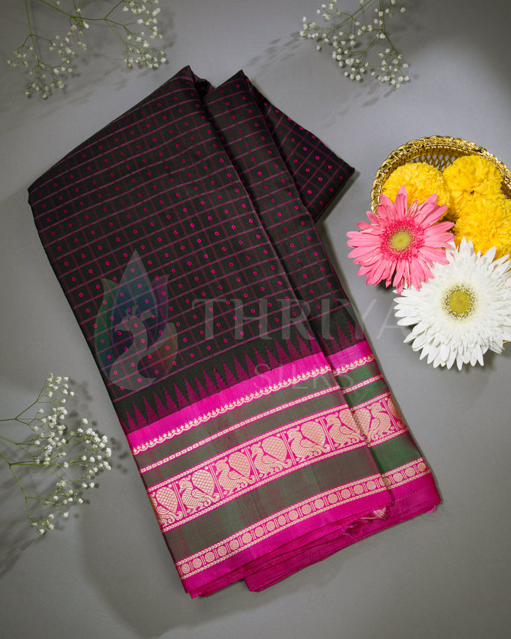 Folded black and pink Kanjivaram silk saree with gold zari border, styled with flowers for presentation