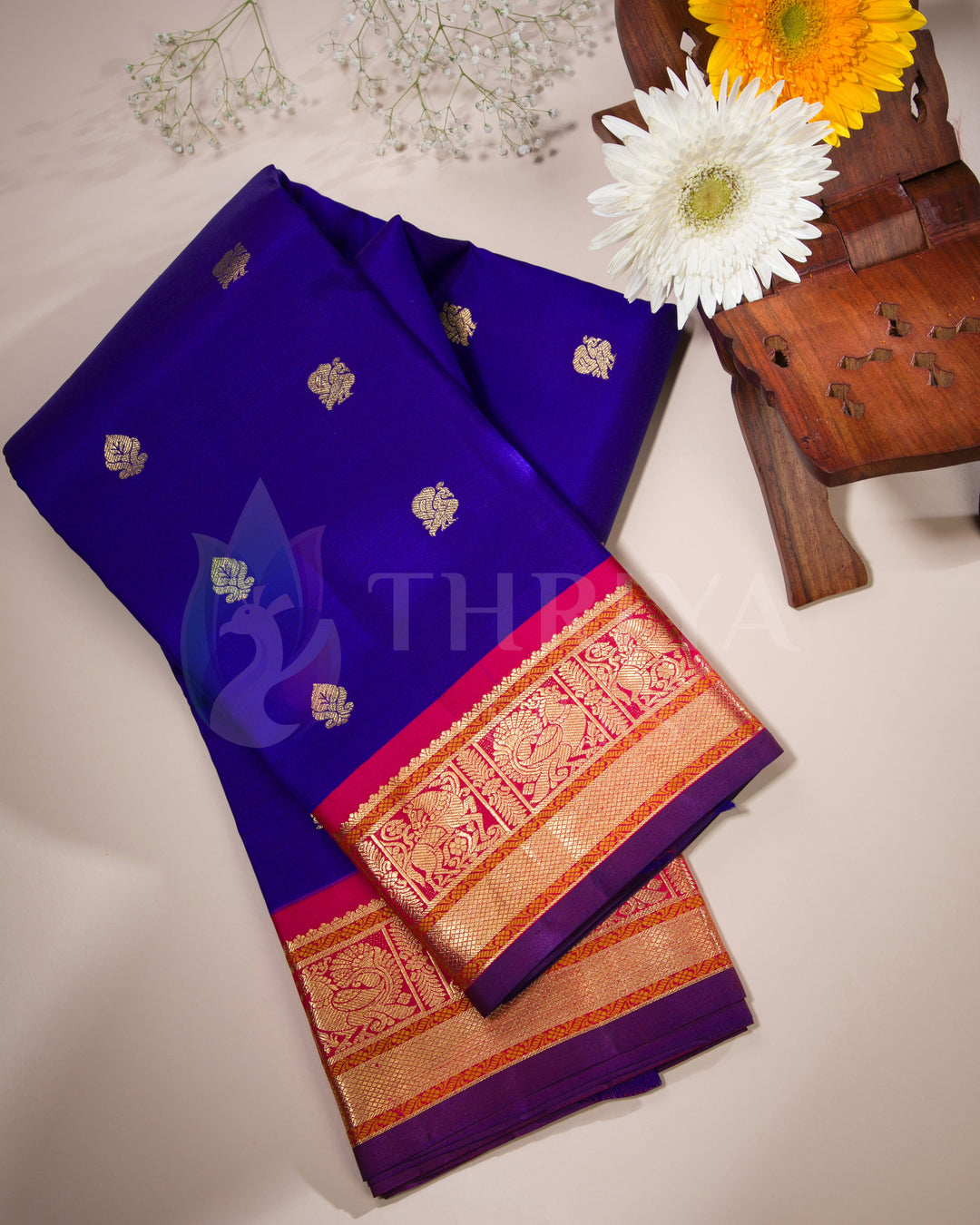 Folded Kanjivaram silk saree in royal blue with golden motifs and rich zari border – lifestyle flat lay from Thriya Silks