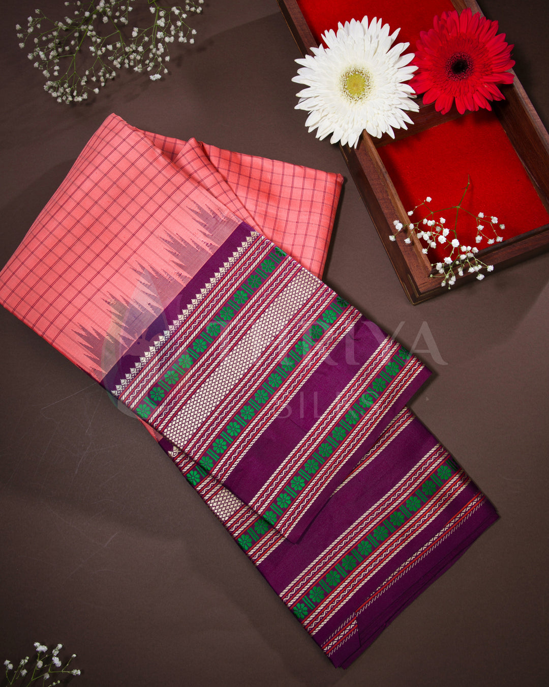 Folded peach and purple Kanjivaram silk saree with green zari work, styled with flowers