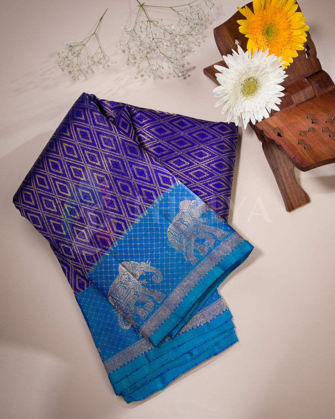 Folded view of purple and peacock blue silk saree with gold elephant border, styled with flowers