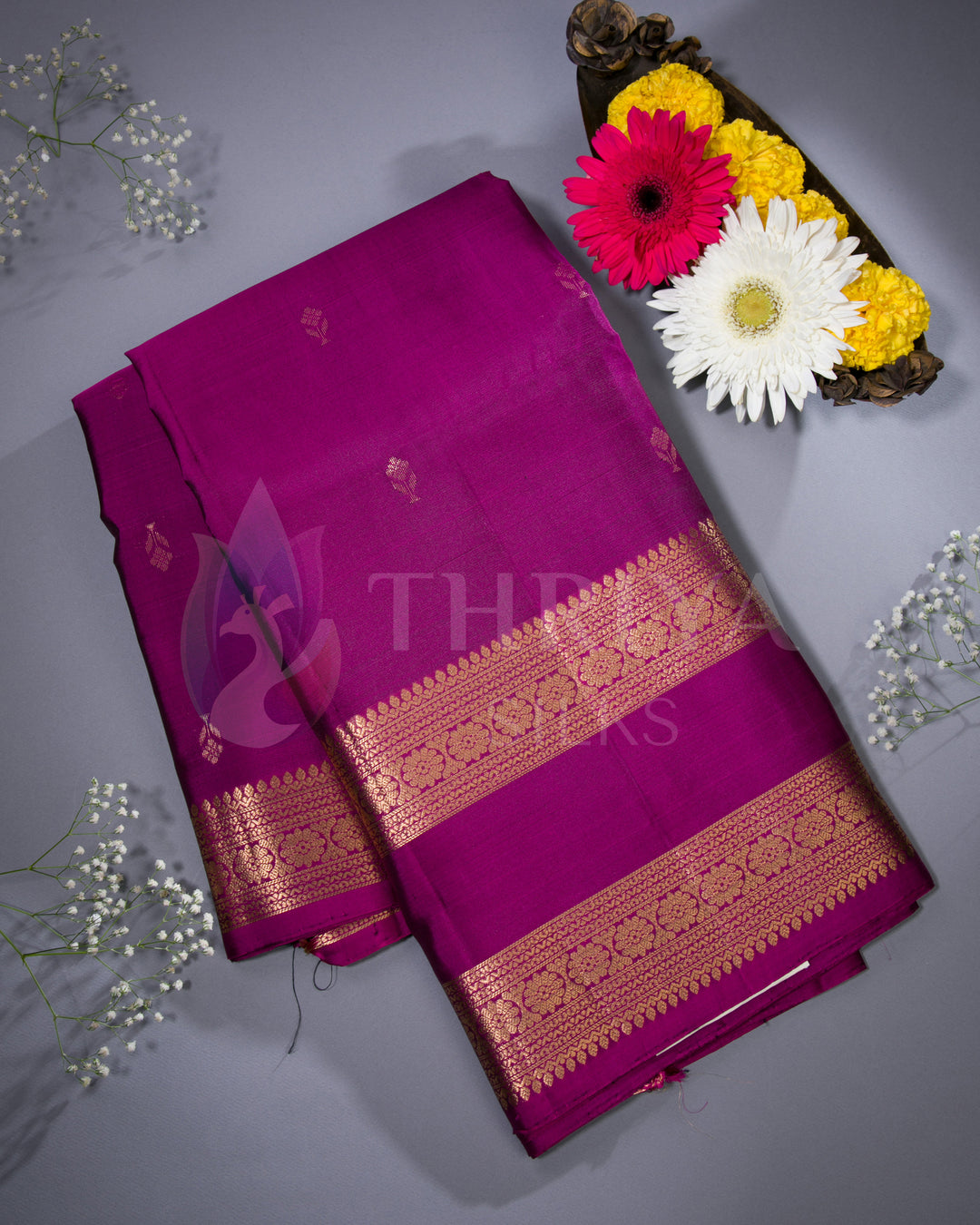 Magenta silk Kanjivaram saree arranged with decorative flowers in a lifestyle shot