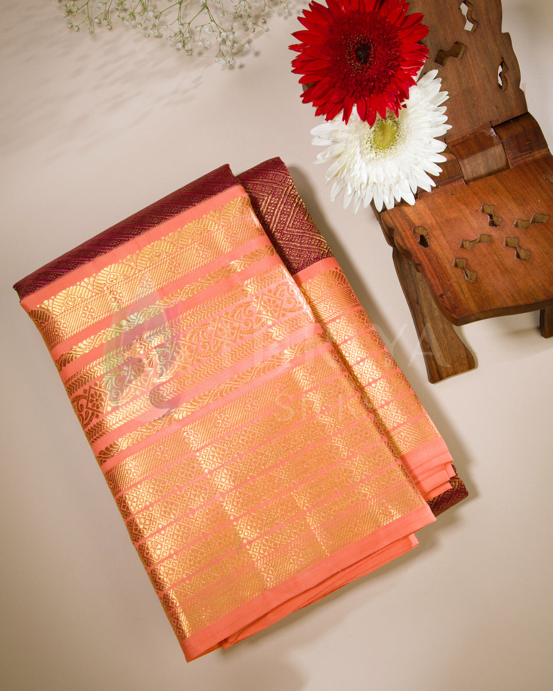 Folded view of peach-orange silk saree featuring gold zari border and rich maroon contrast pallu.