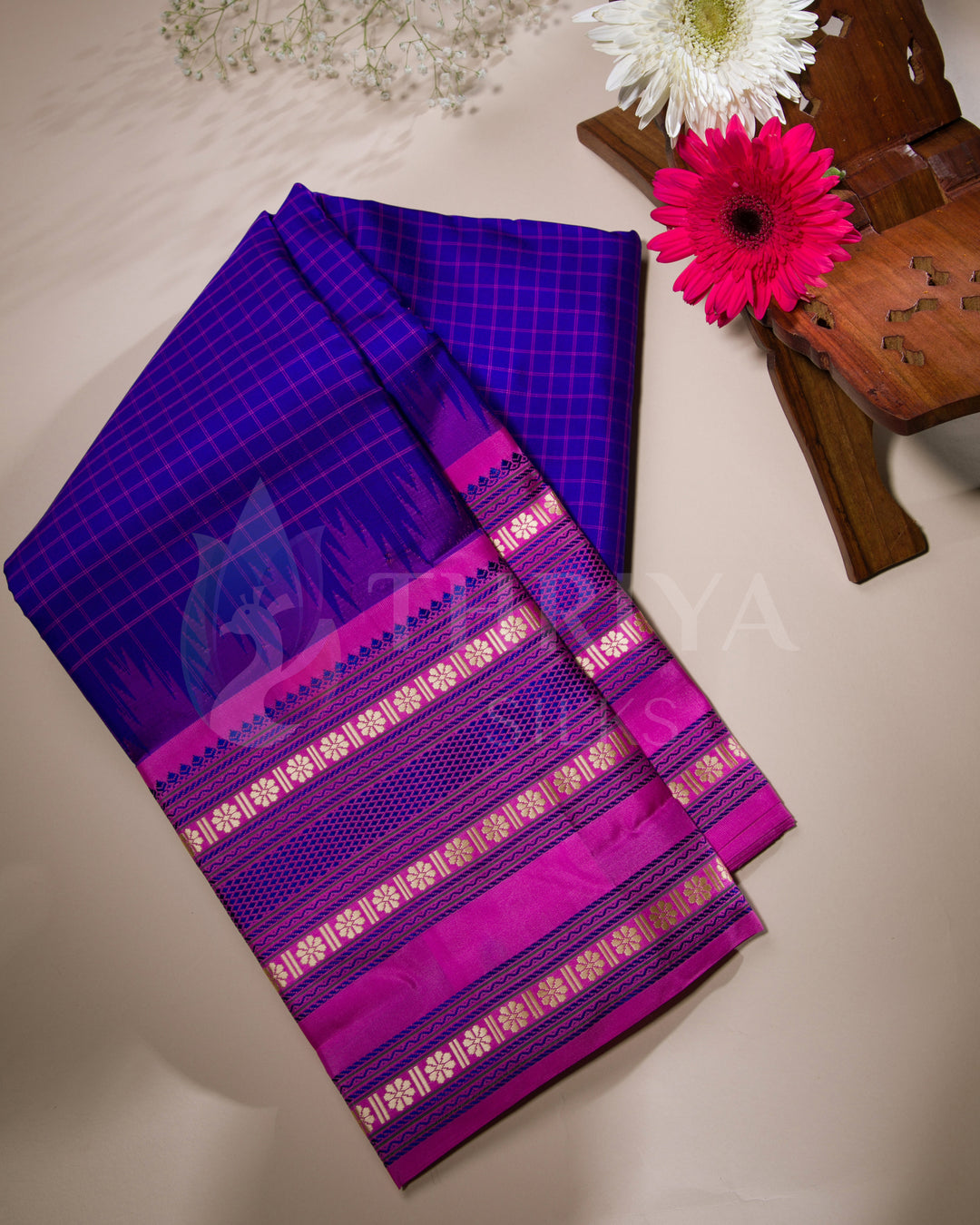 Folded purple and pink silk saree with gold zari border displayed with flowers, from Thriya Silks