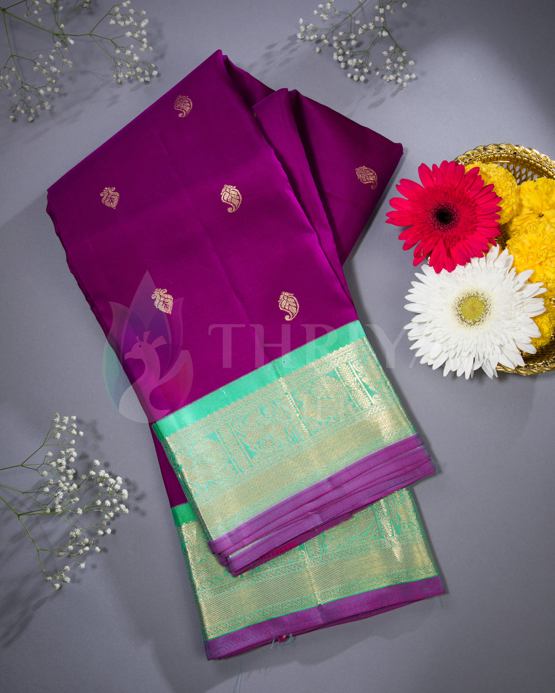 Folded Thriya silk saree in purple with green zari border, styled with flowers for a festive flat lay presentation