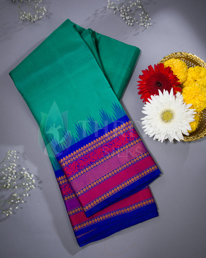 Folded teal green silk saree with royal blue and magenta border – styled flatlay with flowers by Thriya Silks