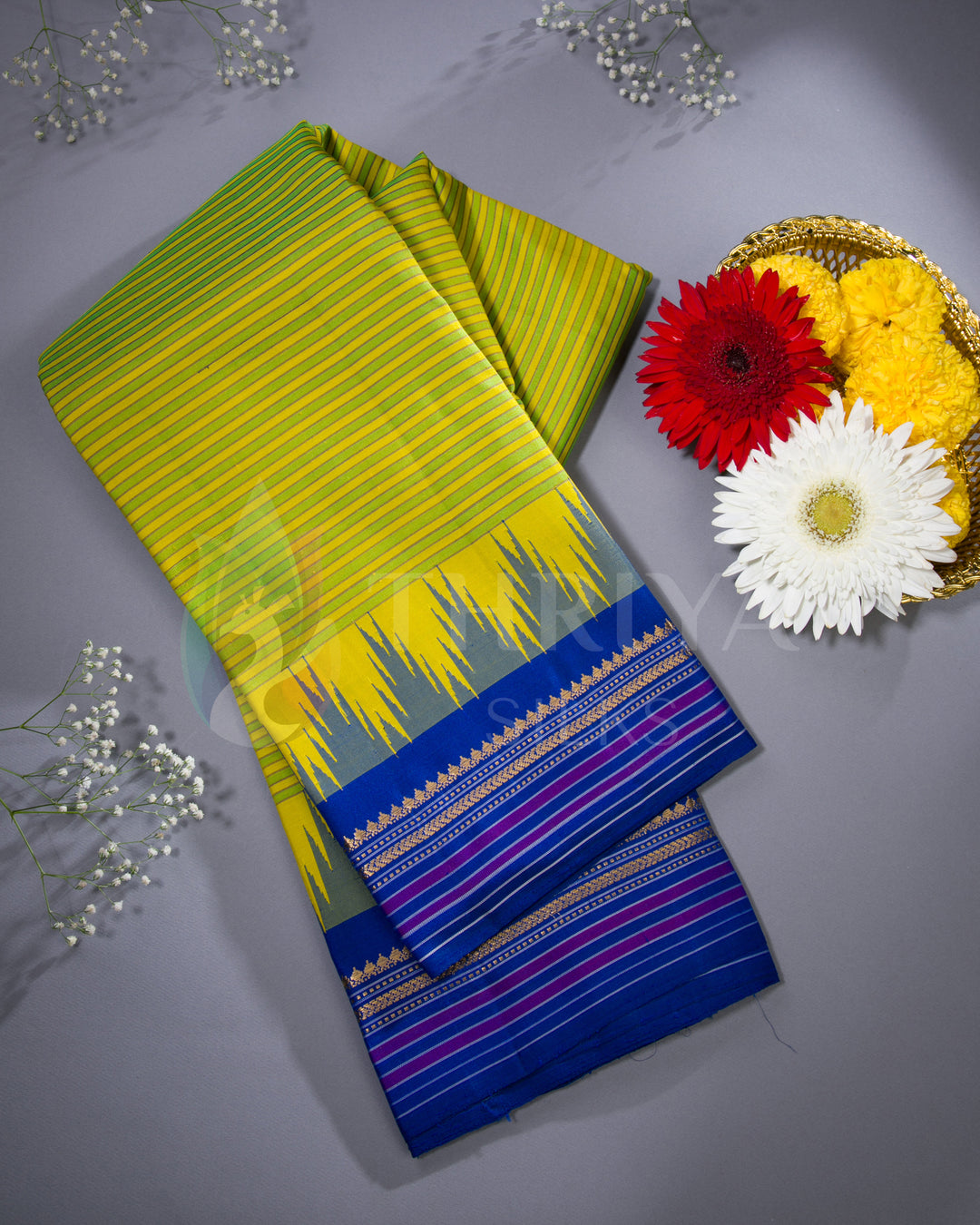 Folded yellow-green and blue silk saree displayed with red, white, and yellow flowers, from Thriya Silks