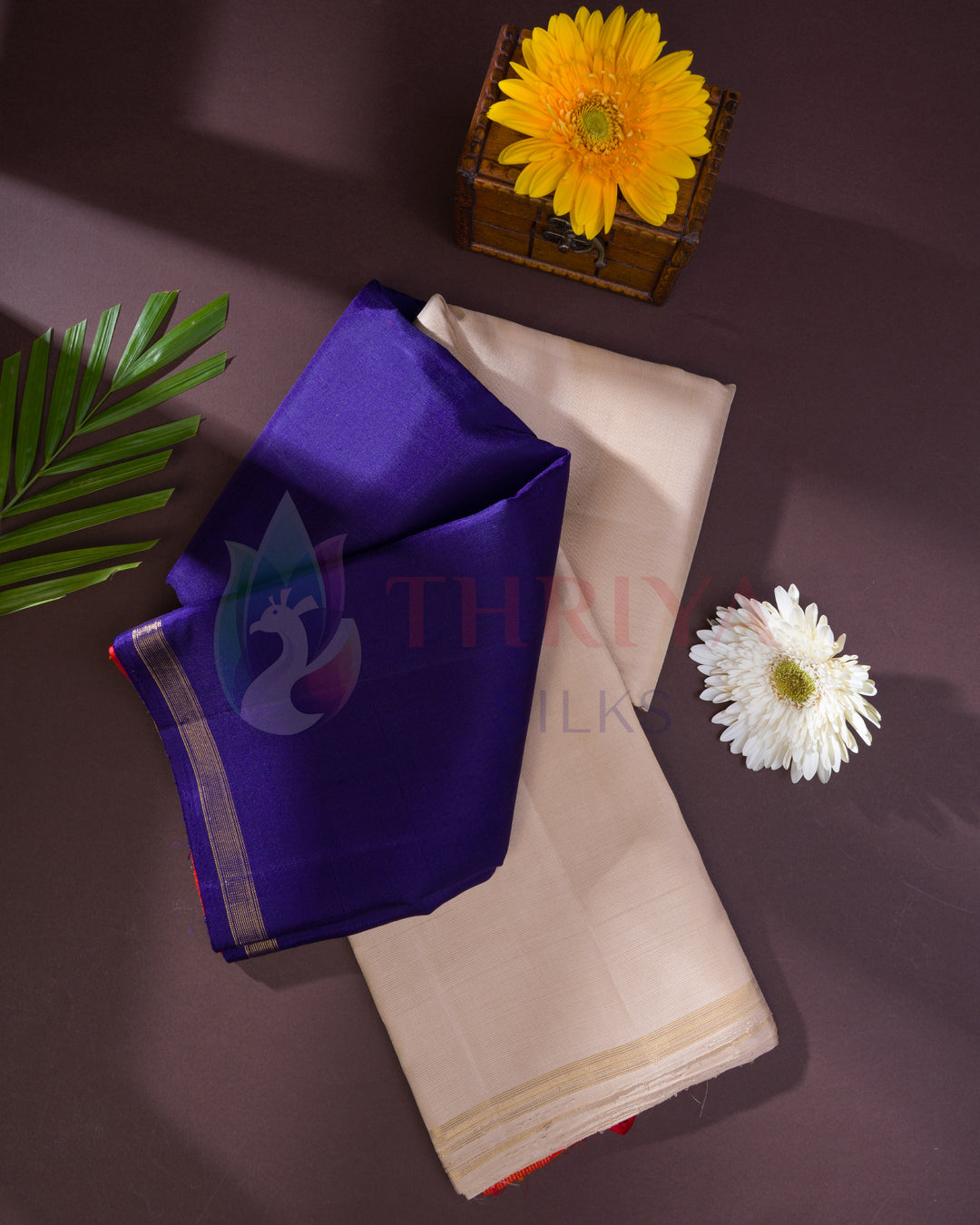 Elegant Kanchipuram silk saree in rich purple and beige with gold zari border, displayed with flowers on a dark background