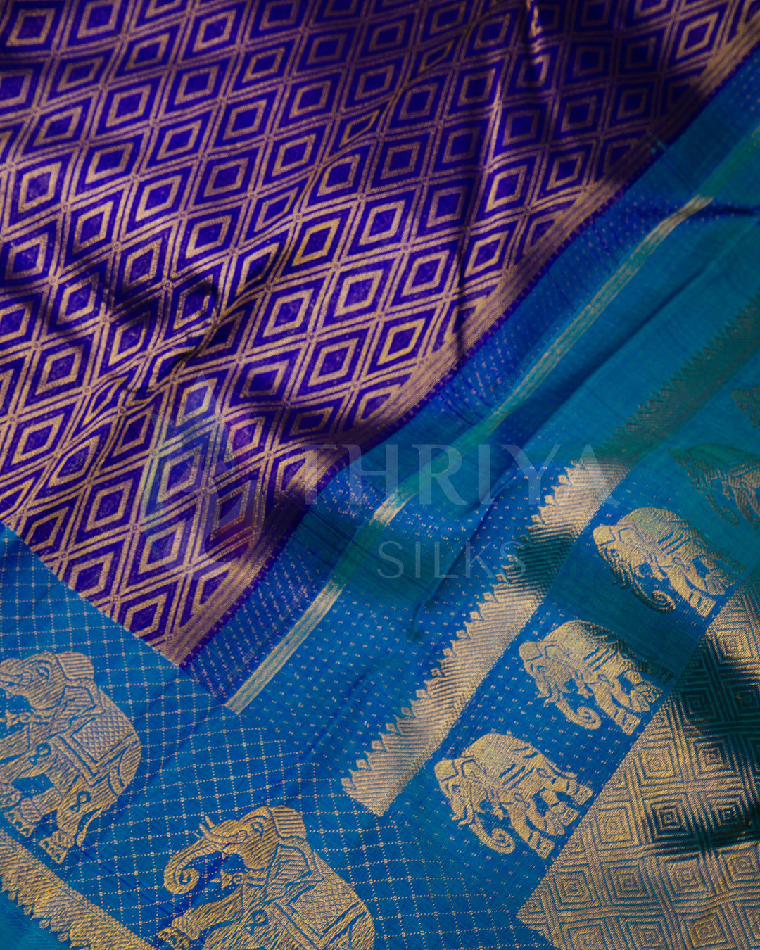 Close-up of purple silk saree with geometric zari patterns and bold peacock blue elephant border