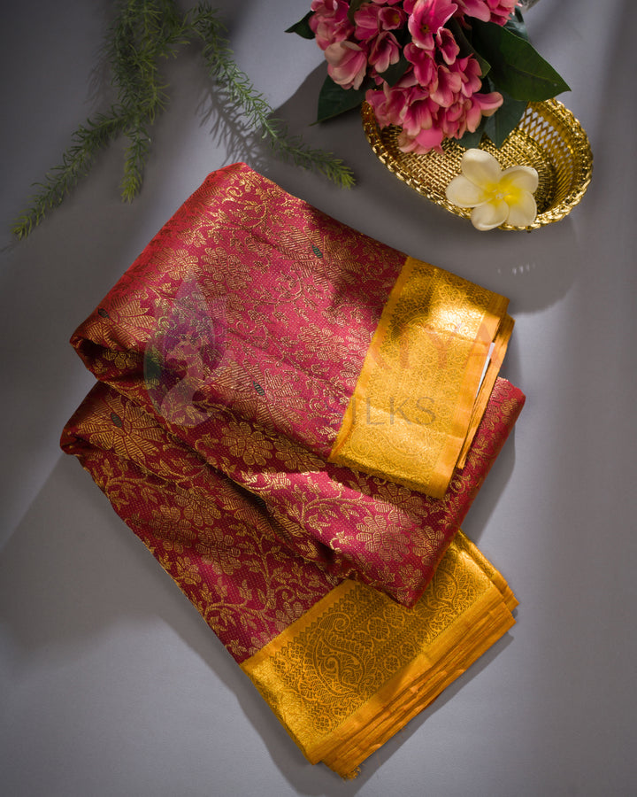 Maroon Kanjivaram silk saree with golden zari border, styled with flowers on a grey background.