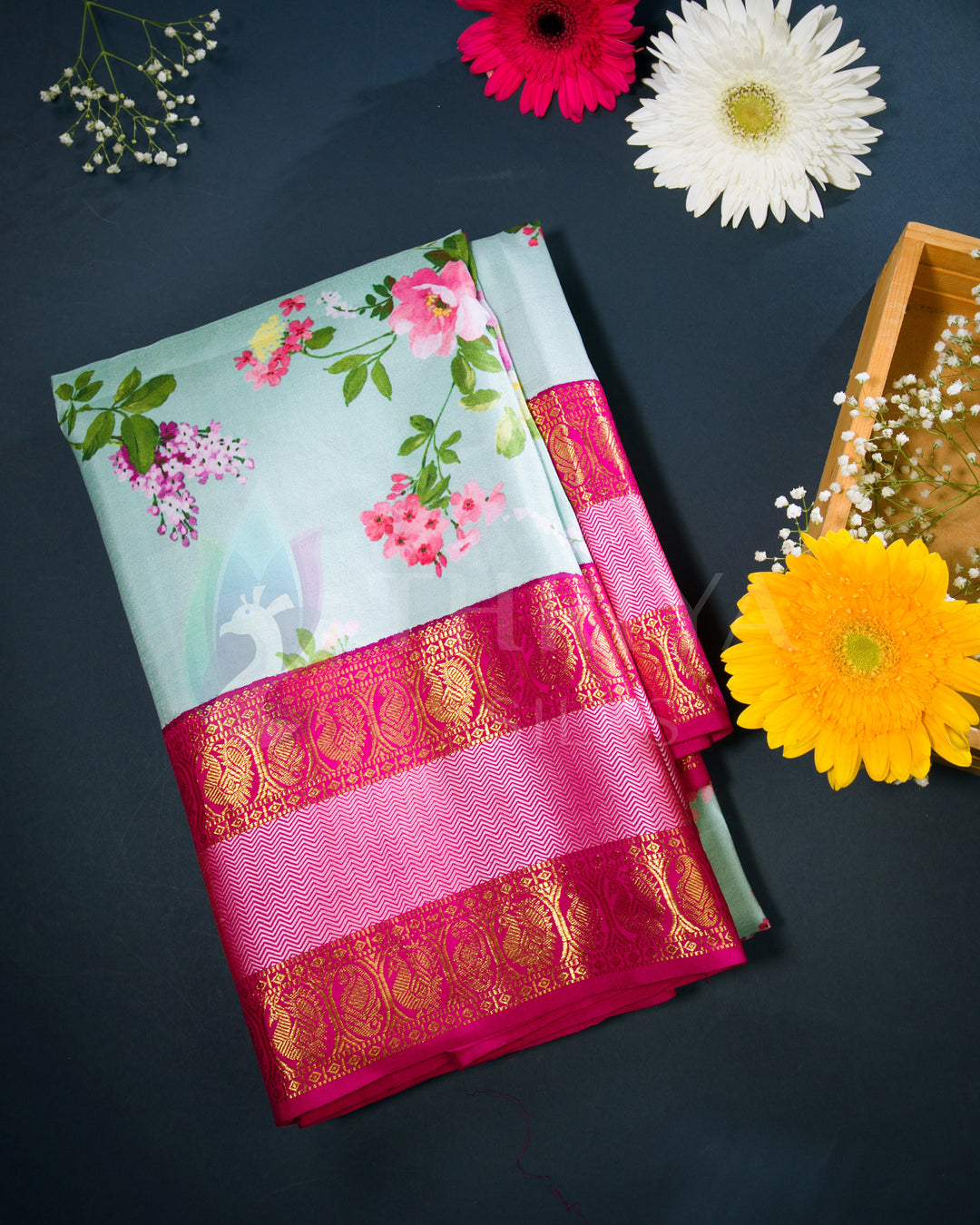 Folded view of mint green silk saree with vibrant floral prints and a broad pink-gold zari border.