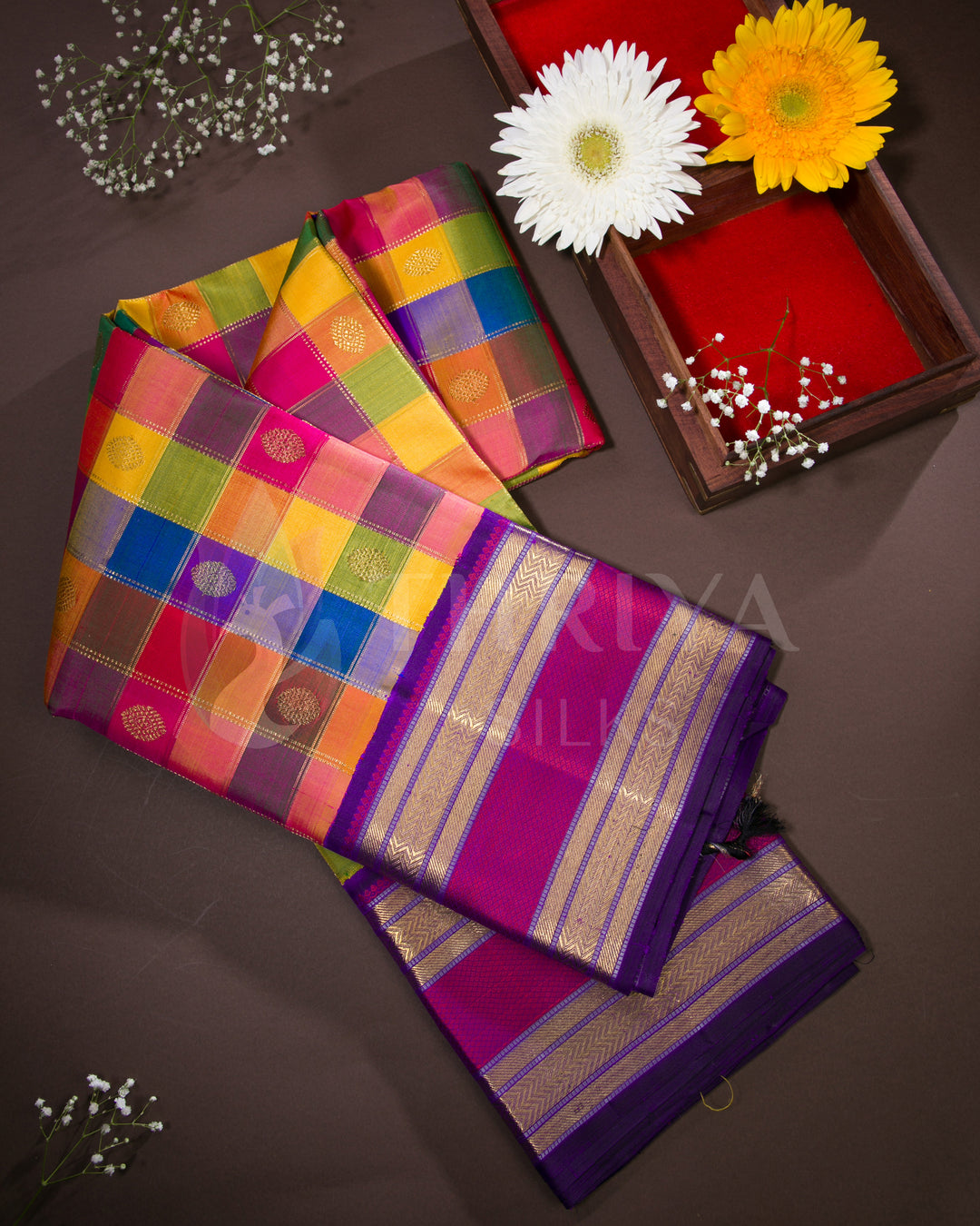 Folded angled flat lay of multicolor checked Kanchipuram silk saree with purple pallu, styled with floral decor for a festive look