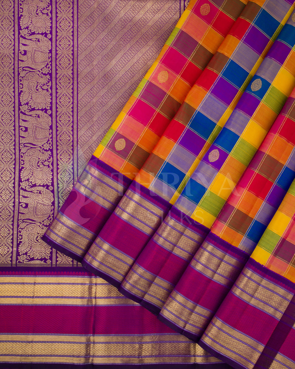 Partially folded flat lay of multicolor checked Kanchipuram silk saree with purple base, featuring rich zari motifs and border