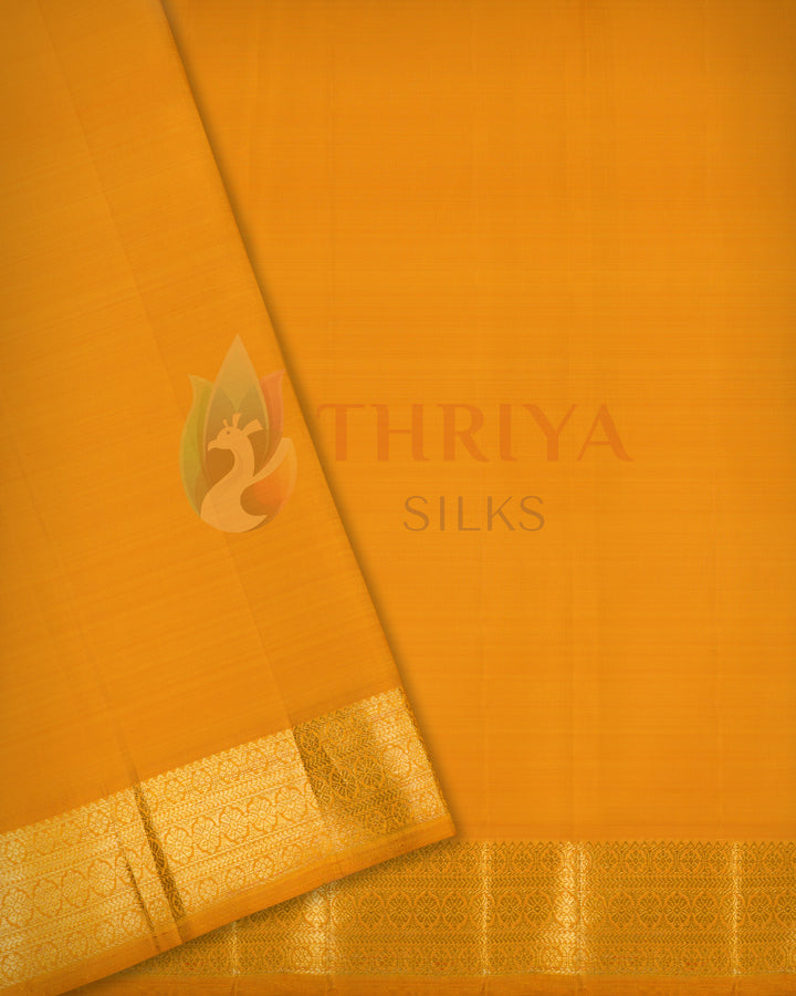 Close-up flat lay of folded mustard yellow Kanchipuram silk saree featuring smooth texture and golden zari border.