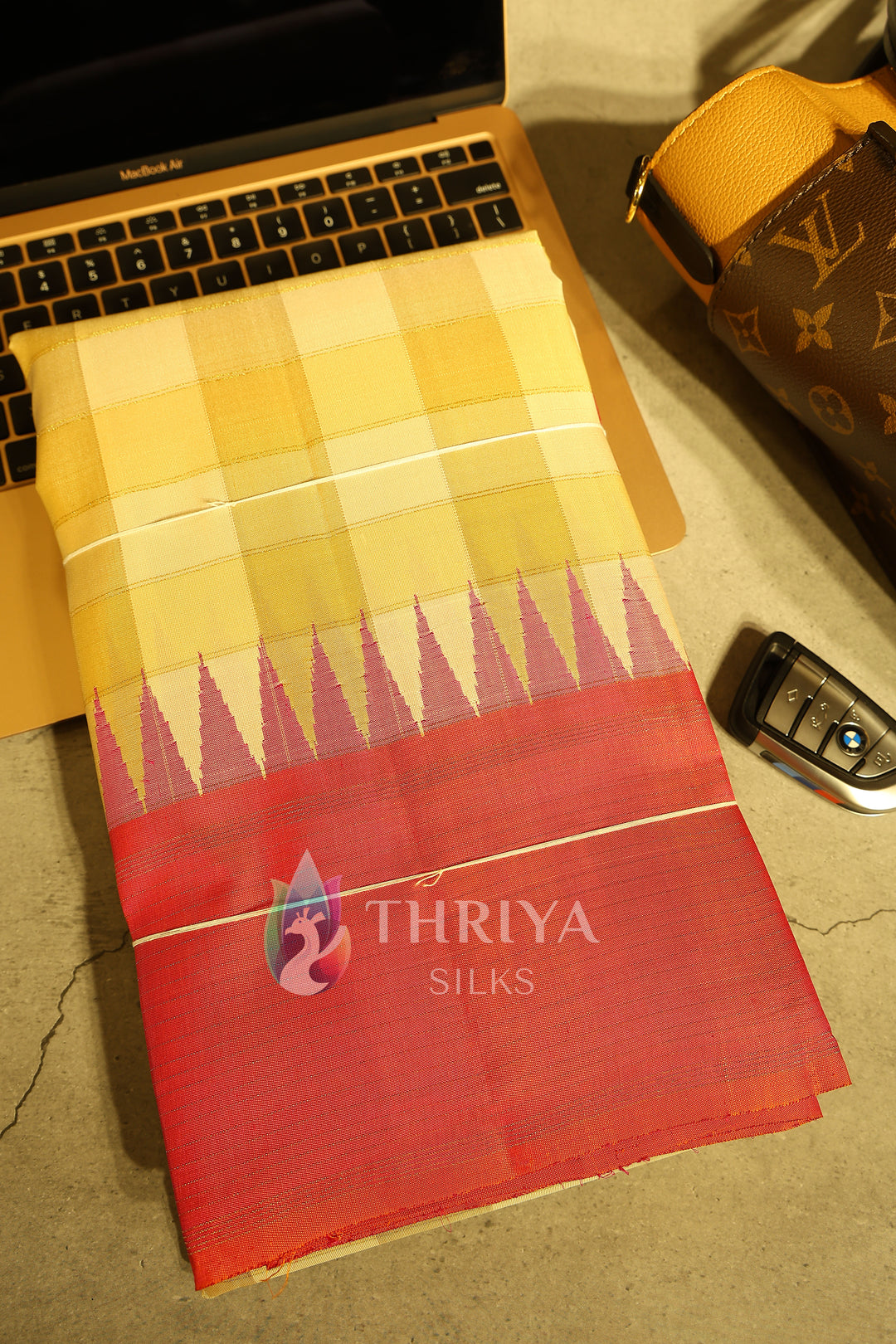 Folded orange and yellow checked silk saree displayed with luxury items.