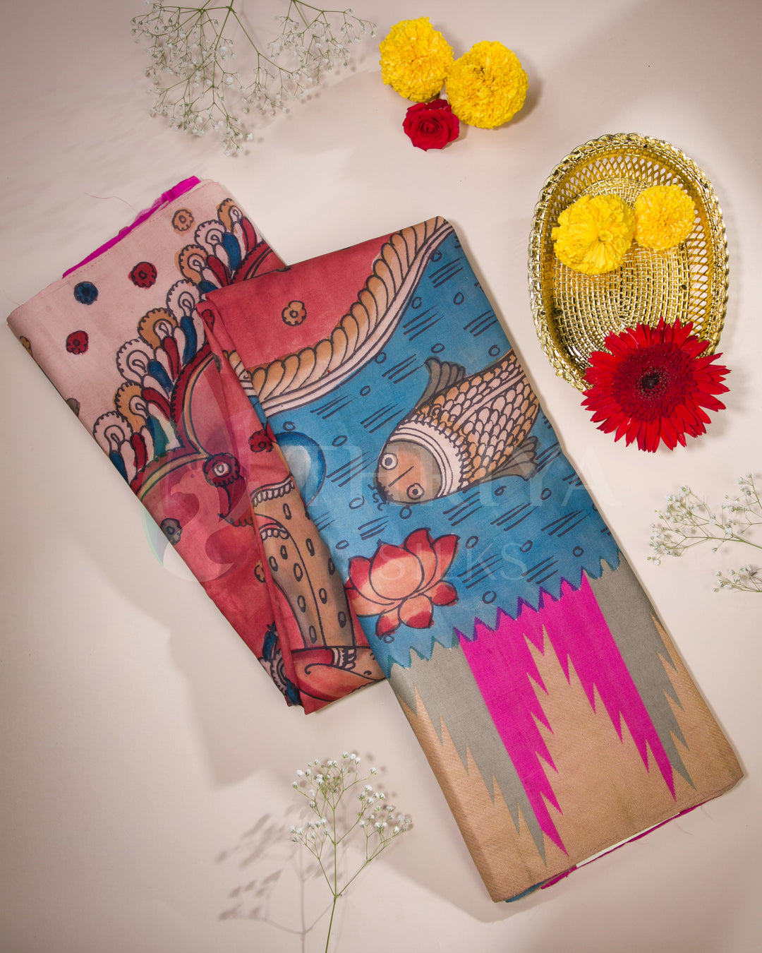 Folded view of pink and blue Kalamkari silk saree with fish and deity motifs, paired with golden zari detailing.