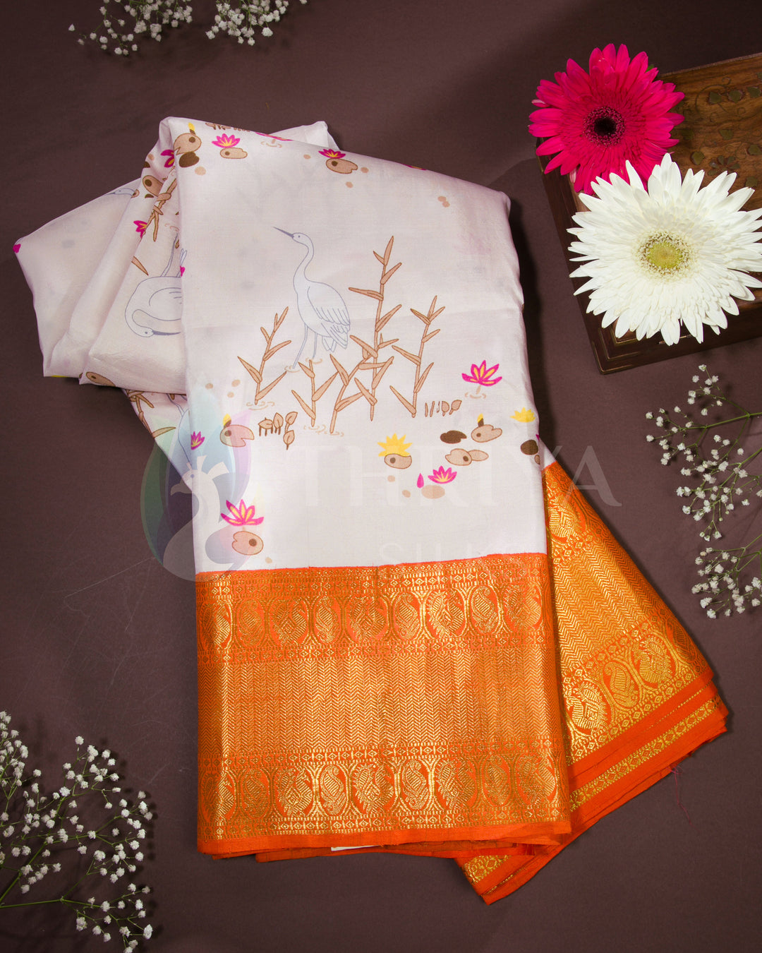 Folded view of pastel pink silk saree with bird and lotus motifs, finished with a rich orange zari border.
