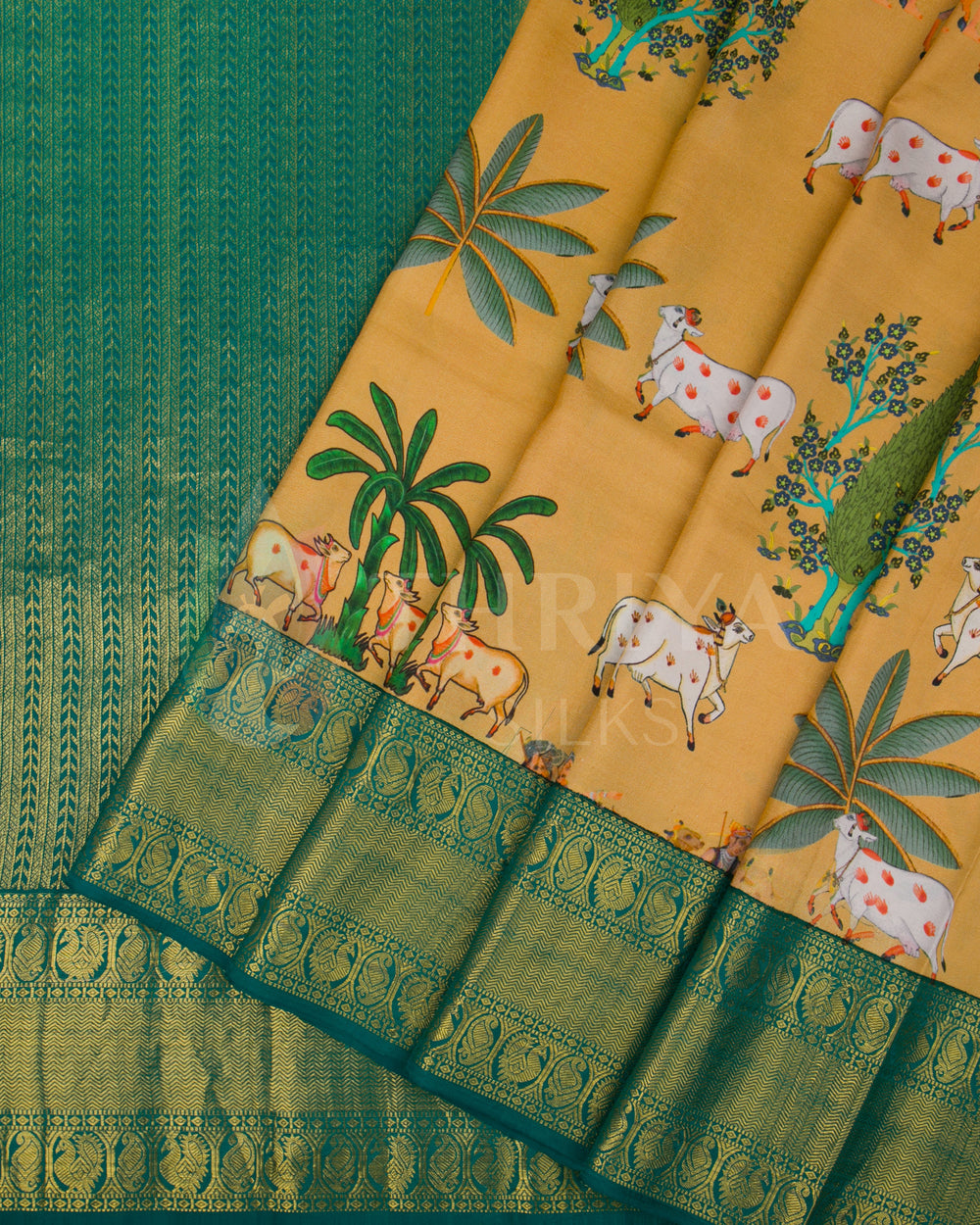 Pleated view showcasing cow motif design on mustard yellow base with green zari border and pallu.