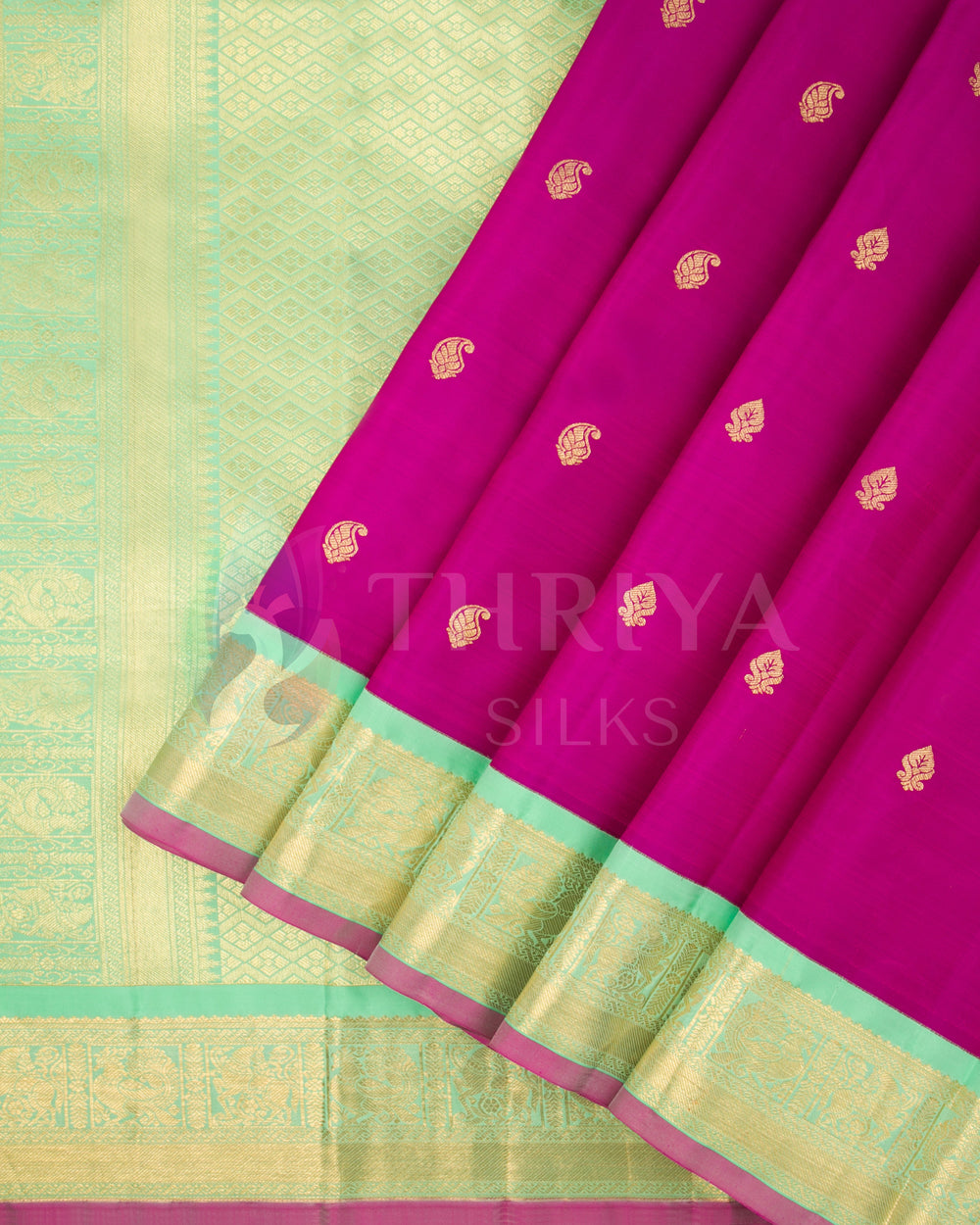 Pleats view of rani pink silk saree with gold motifs and light green zari border finished with pink selvedge