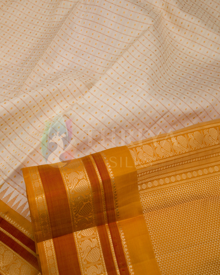 Close-up of cream silk saree with intricate gold zari and dual-tone orange border