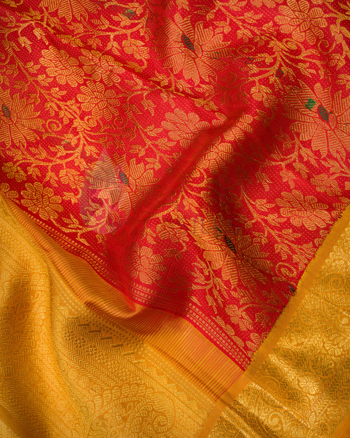 Close-up detailed view of red and gold Kanchipuram silk saree fabric showing intricate floral zari work and rich golden border texture