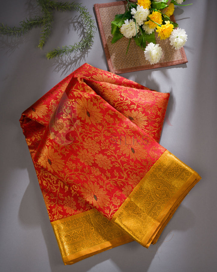 Red and gold Kanchipuram silk saree folded at an angled flat lay with floral arrangement, highlighting rich zari work and vibrant color.
