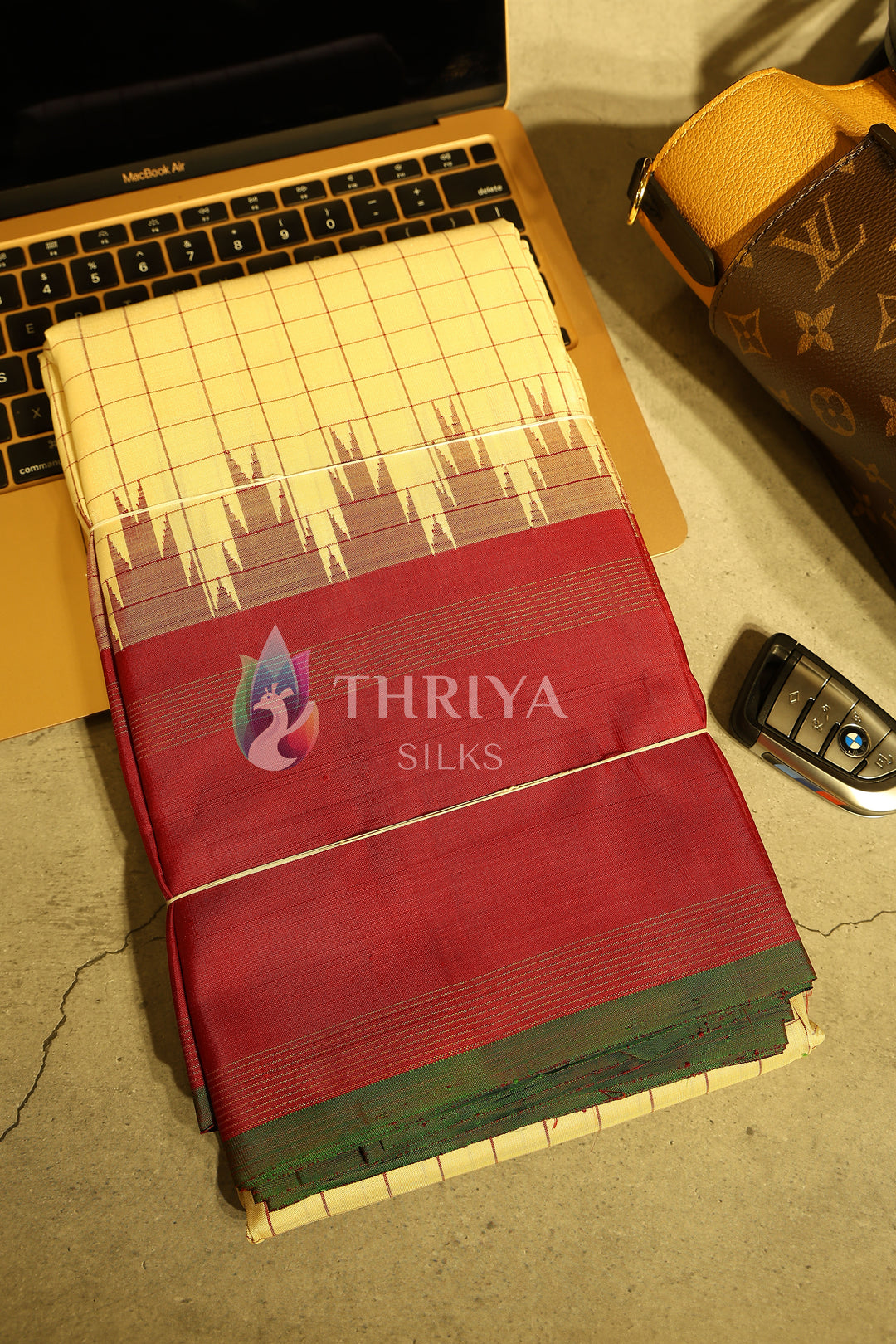 Folded red and cream silk saree showcased with a car key and laptop for luxury styling.