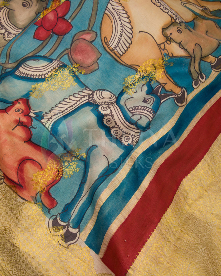 Close-up of golden zari border on sky blue Kalamkari silk saree with animal motifs.
