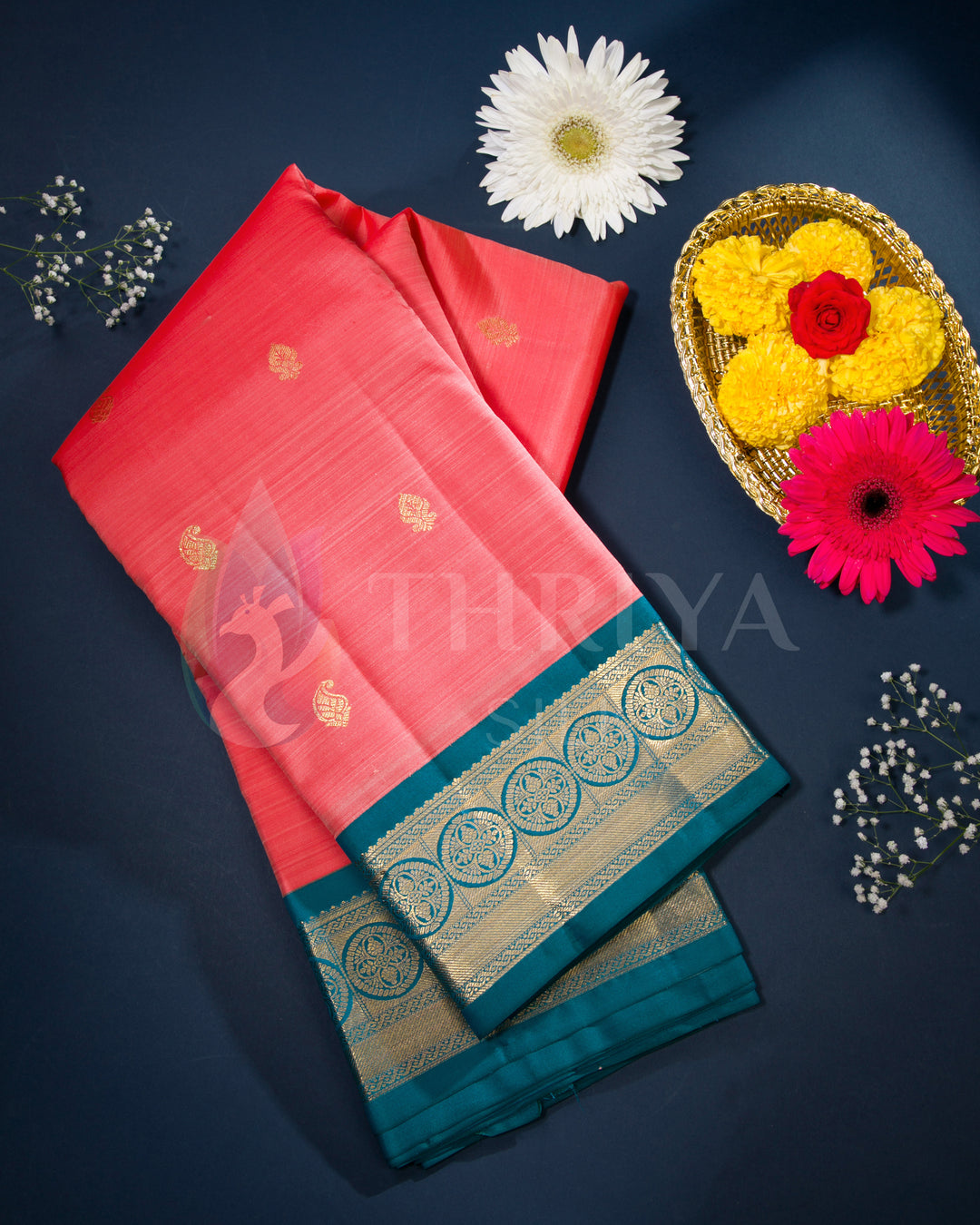Styled display of coral pink silk saree with teal border and intricate zari work